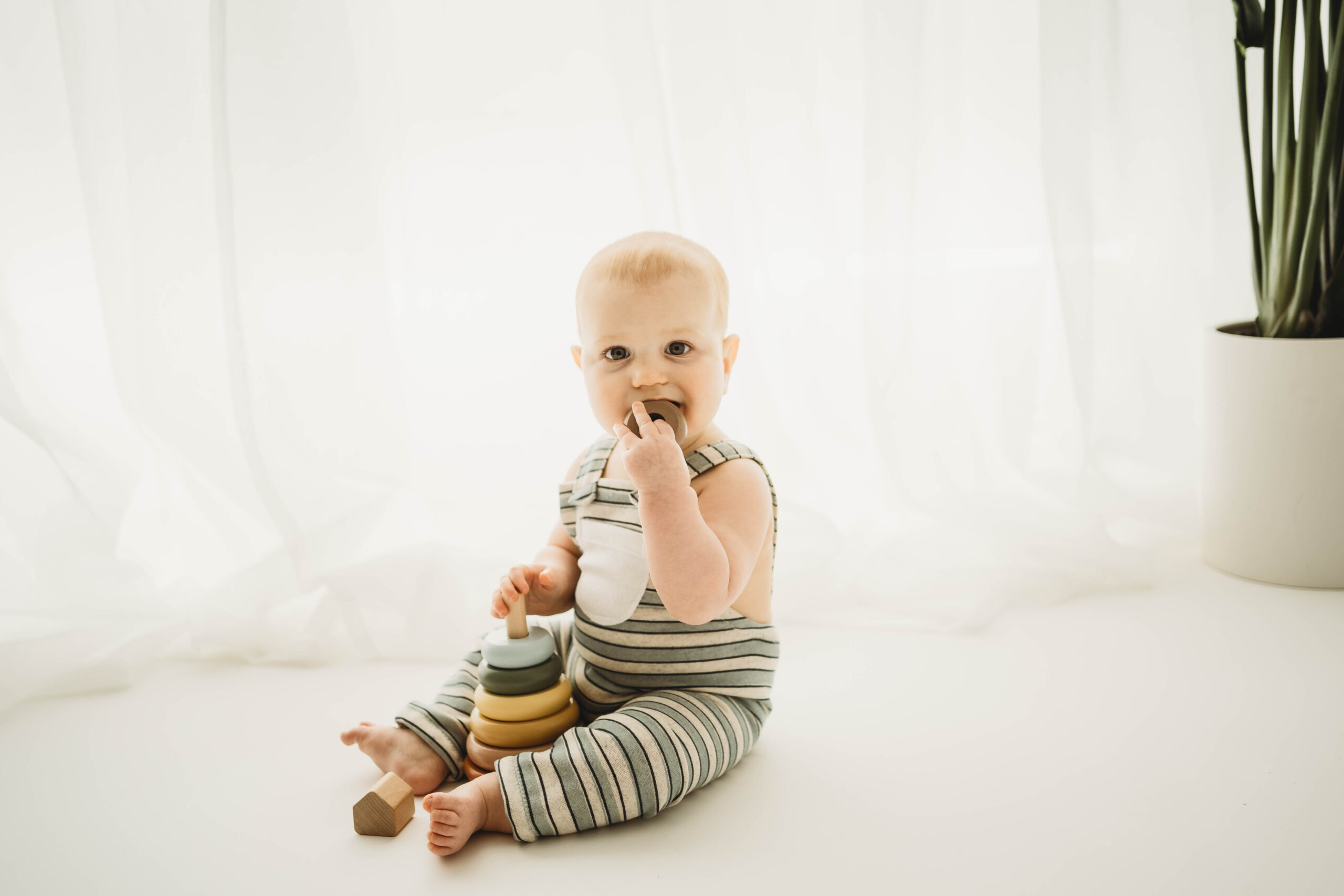 baby wearing striped overalls playing with wooden stacking ring toy.