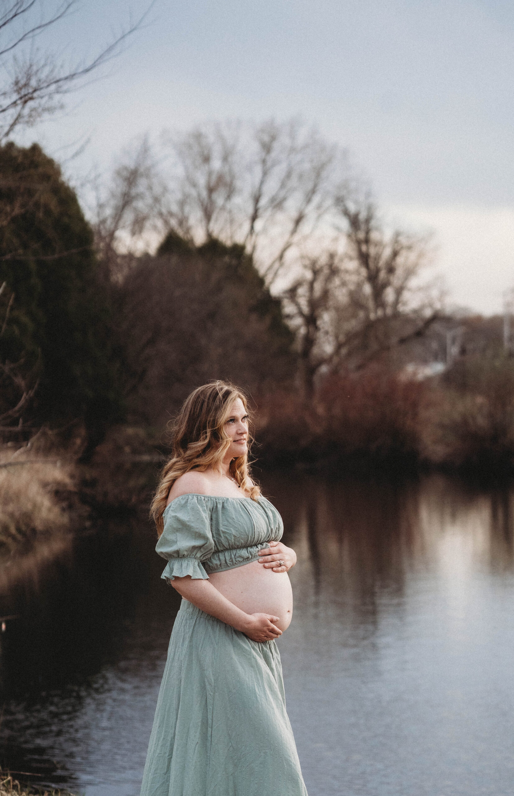 Expecting mom wearing a two piece outfit- standing near a lake.