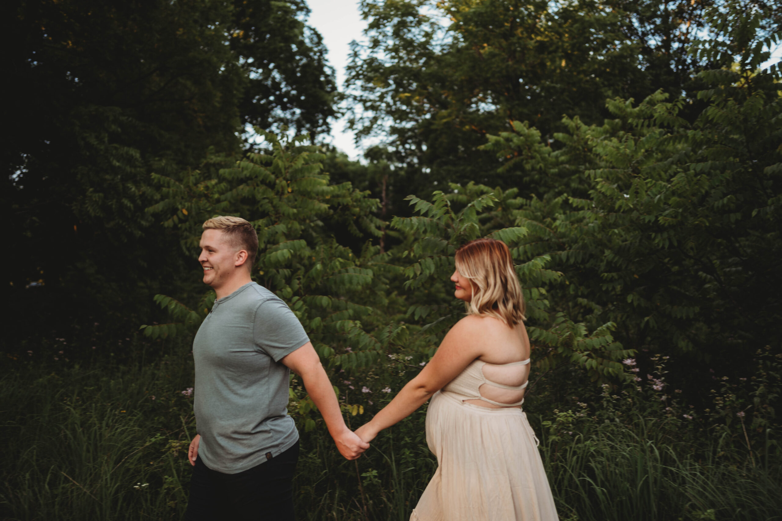 couple holding hands and walking in the woods for their outdoor maternity session.