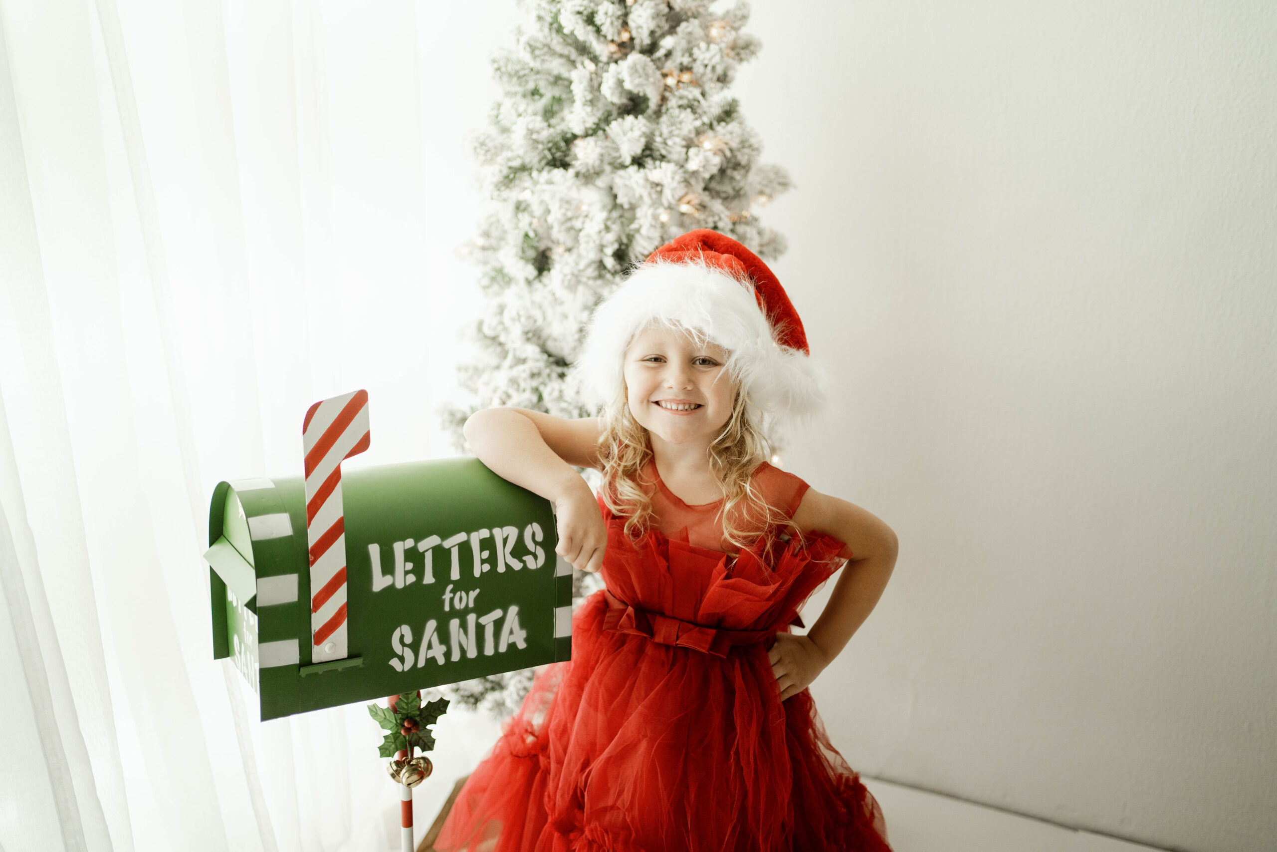 girl in red dress standing with a mailbox for letters to santa.