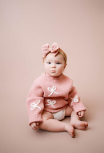 One year old girl with red hair wearing a pink sweater with white bows for her one year portraits. 