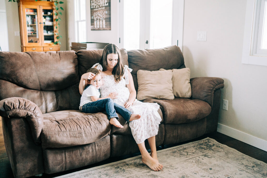 expecting woman snuggling son on a brown couch in their in home maternity session