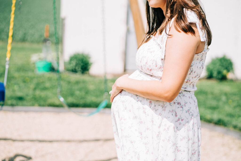 pregnant woman wearing a white floral dress standing outdoors for her lifestyle maternity session