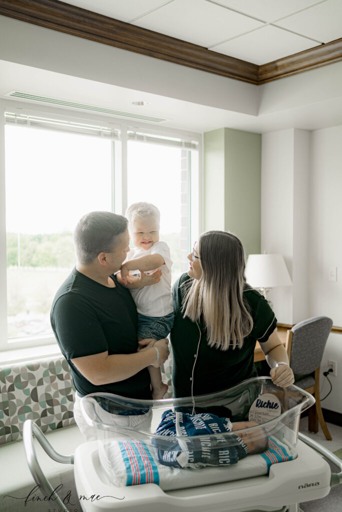 mom, dad and big brother looking in the hospital bassinet at a newborn baby brother at a fresh 48 hospital session near madison wi