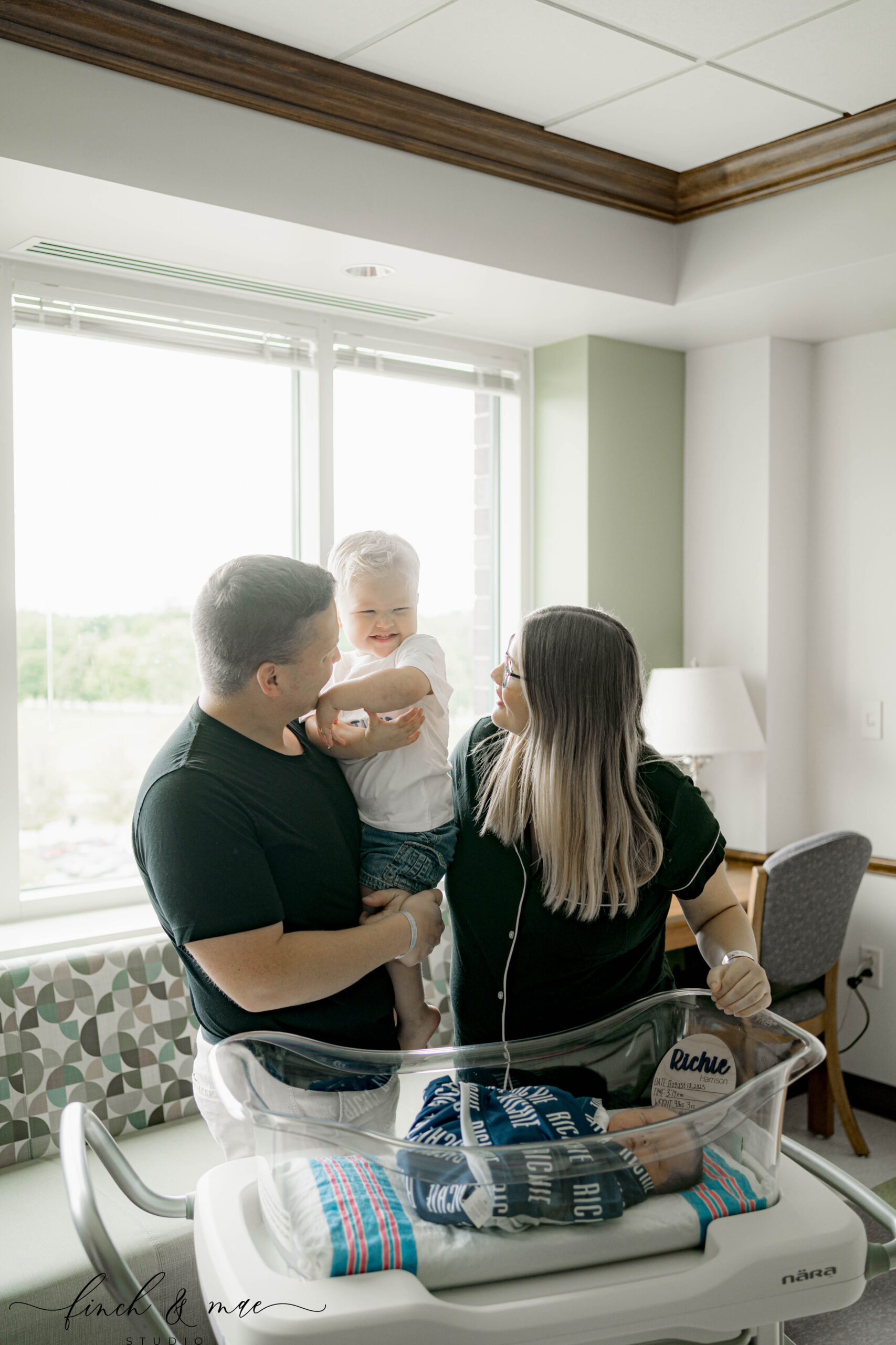 mom, dad and big brother looking in the hospital bassinet at a newborn baby brother at a fresh 48 hospital session near madison wi