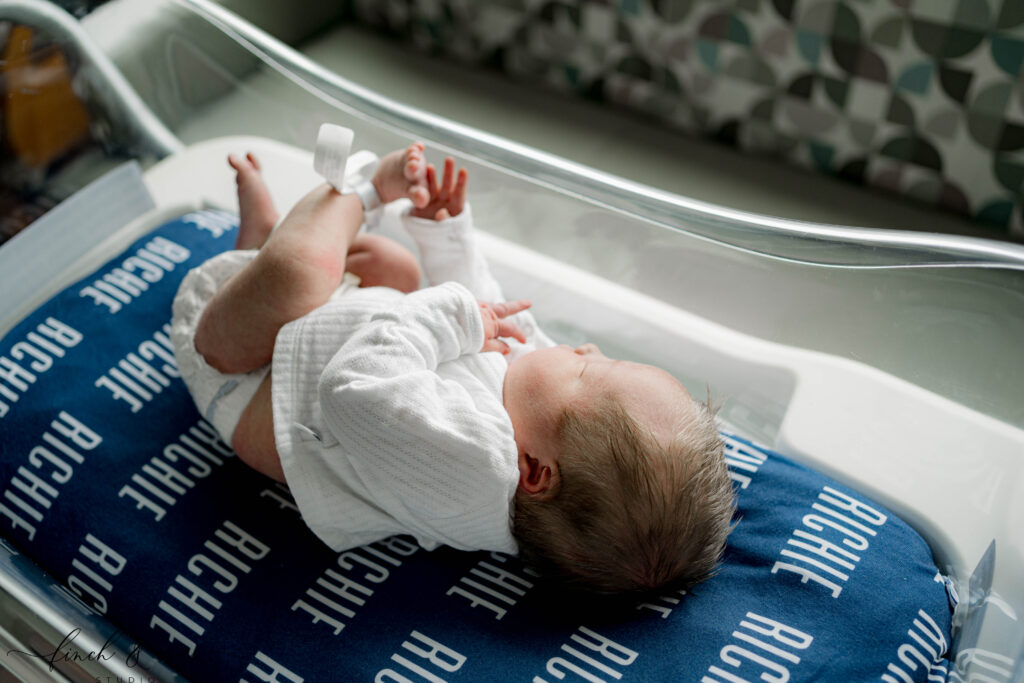 Newborn baby lying in hospital bassinet on a personalized navy “Richie” blanket during Fresh 48 hospital session in Madison, Wisconsin.