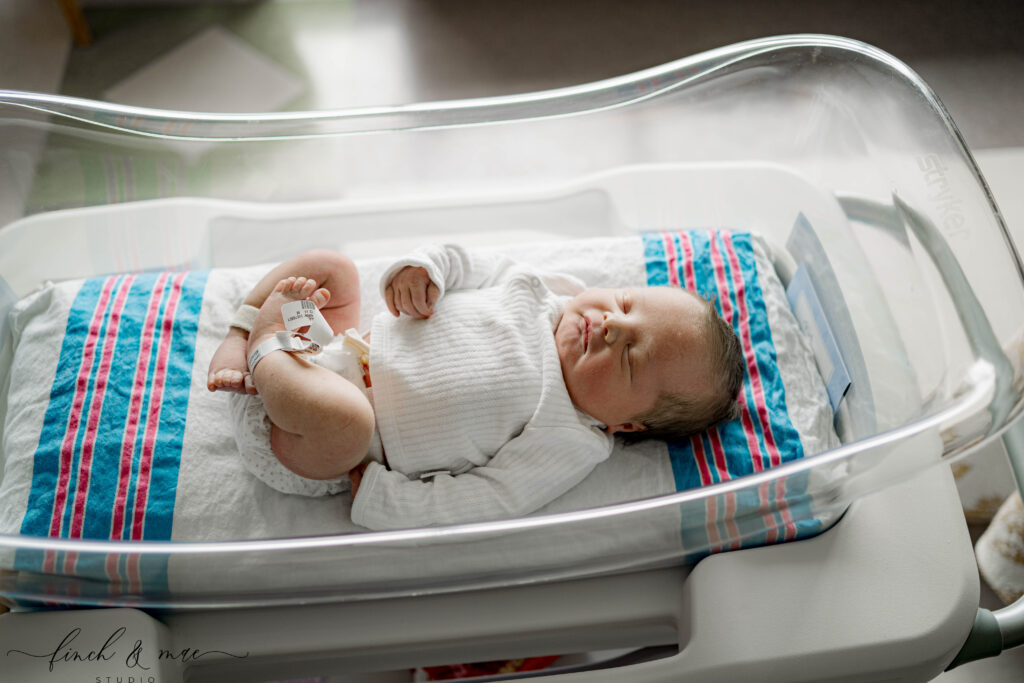 Newborn baby resting in hospital bassinet with striped hospital blanket during Fresh 48 photography session in Madison, Wisconsin.