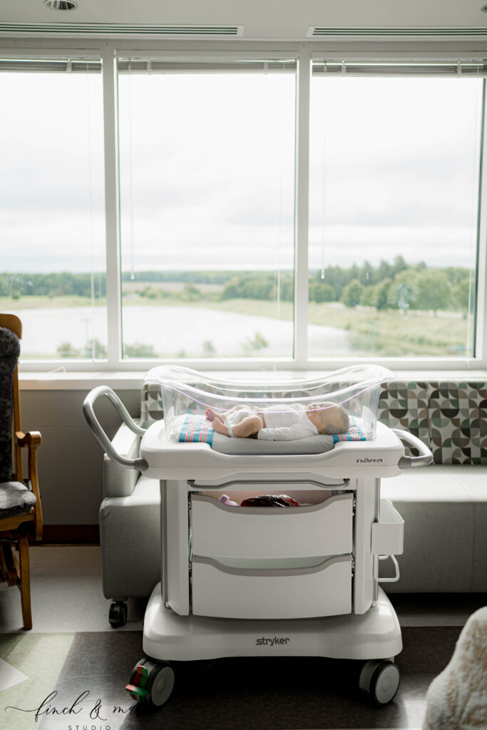 Newborn baby resting in hospital bassinet near window during Fresh 48 photography in Sun Prairie, WI.