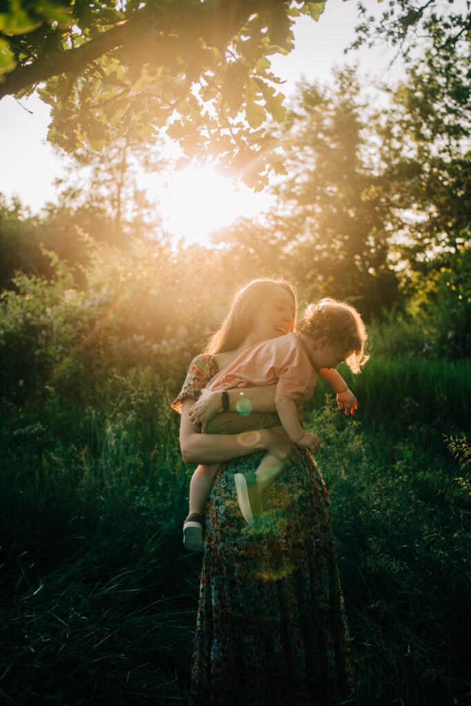 Mother holding toddler close and laughing in a sunlit field during family photography session.