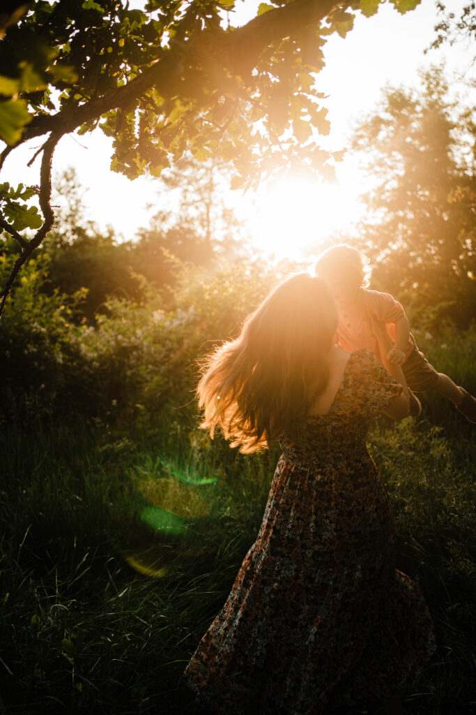 Mother spinning with toddler in her arms beneath glowing sunset light.
