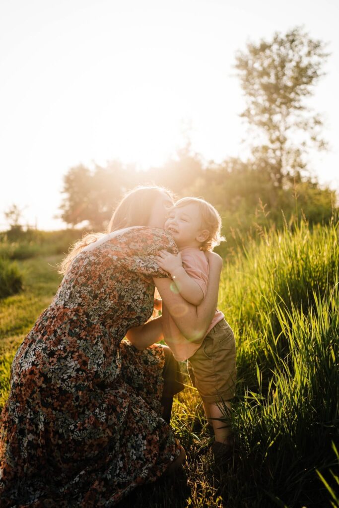 Toddler hugging mother in the grass with golden sunset light behind them.