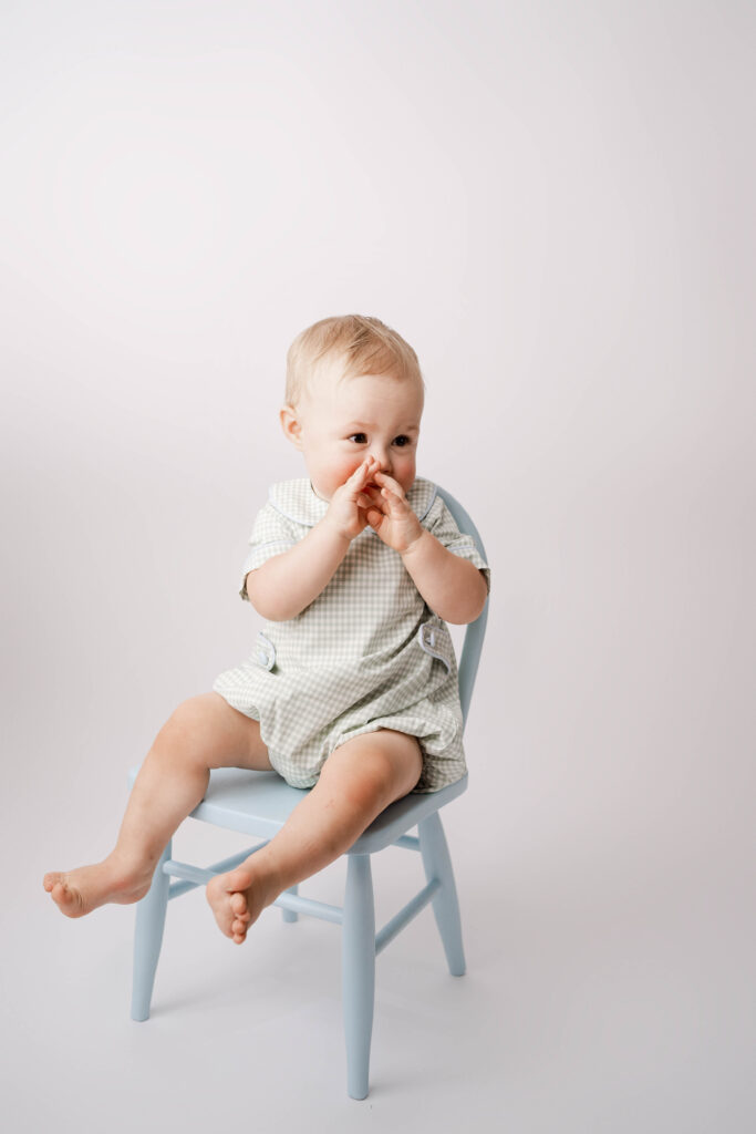 one year old boy sitting on a blue chair in a green and white checkered outfit.