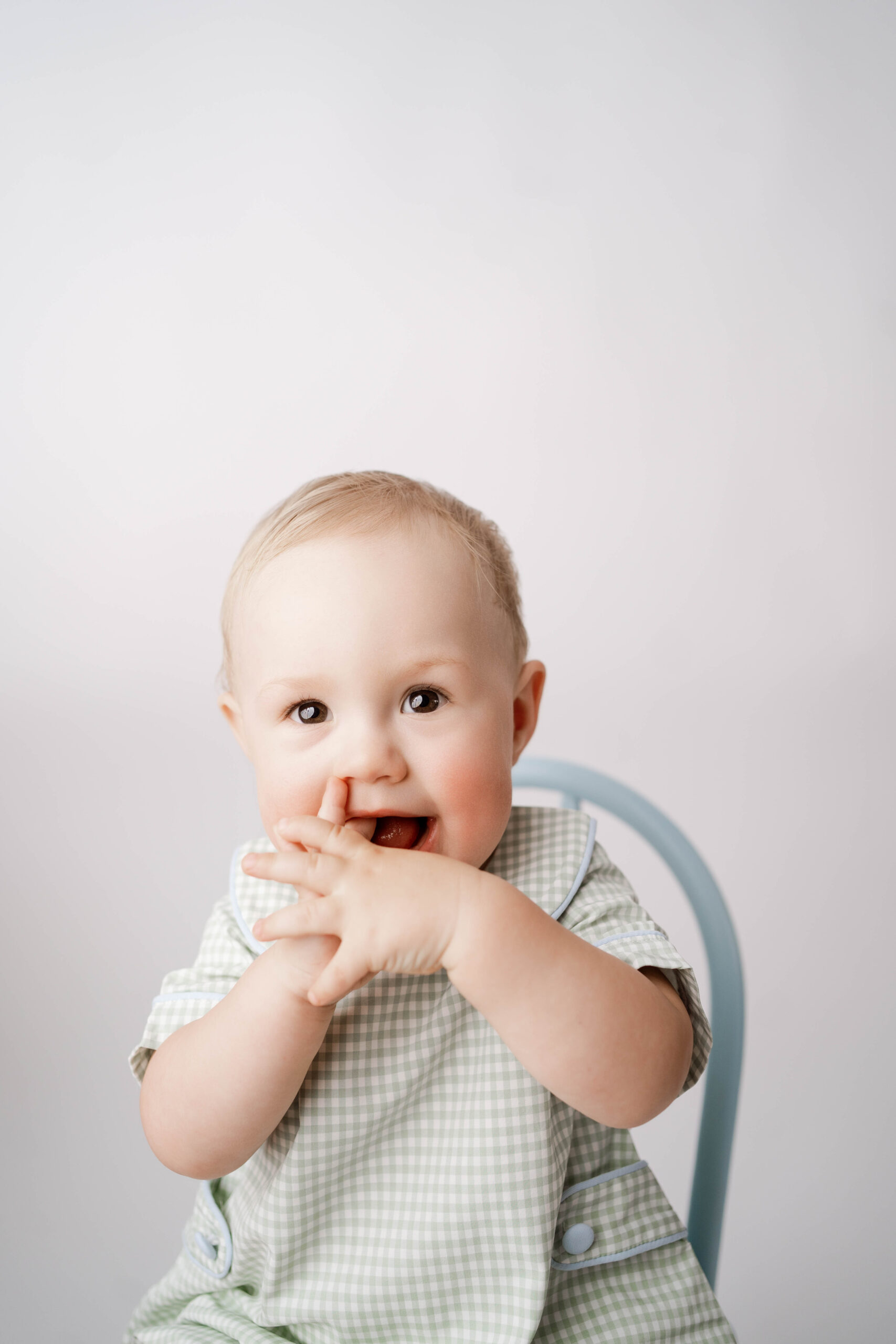 one year old boy playing with his fingers during his one year portrait session.