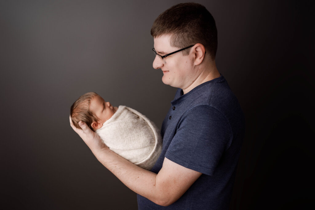 dad smiling down at his newborn son during their newborn session in rio, wi