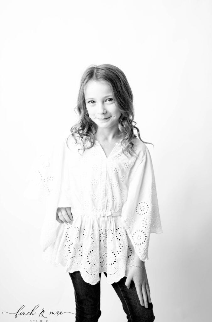 Full-length studio portrait of a young girl in eyelet blouse, posed sweetly with hands on hip, fine art child photography in Madison WI.