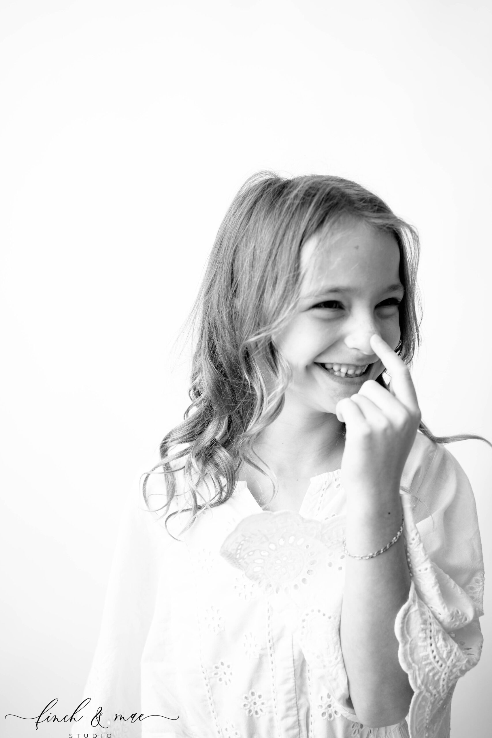 Laughing candid of a girl touching her nose, playful black and white children’s portrait in Rio WI photography studio.