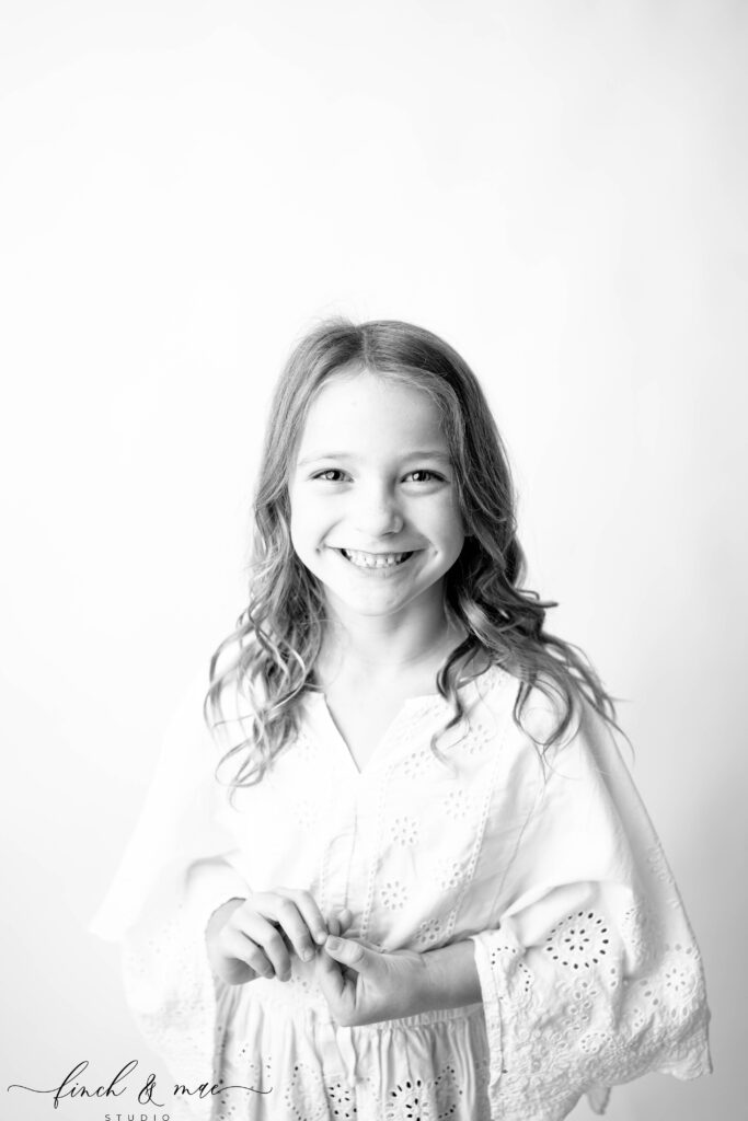 Classic child portrait of a young girl smiling softly at the camera, timeless black and white studio photography in Wisconsin.