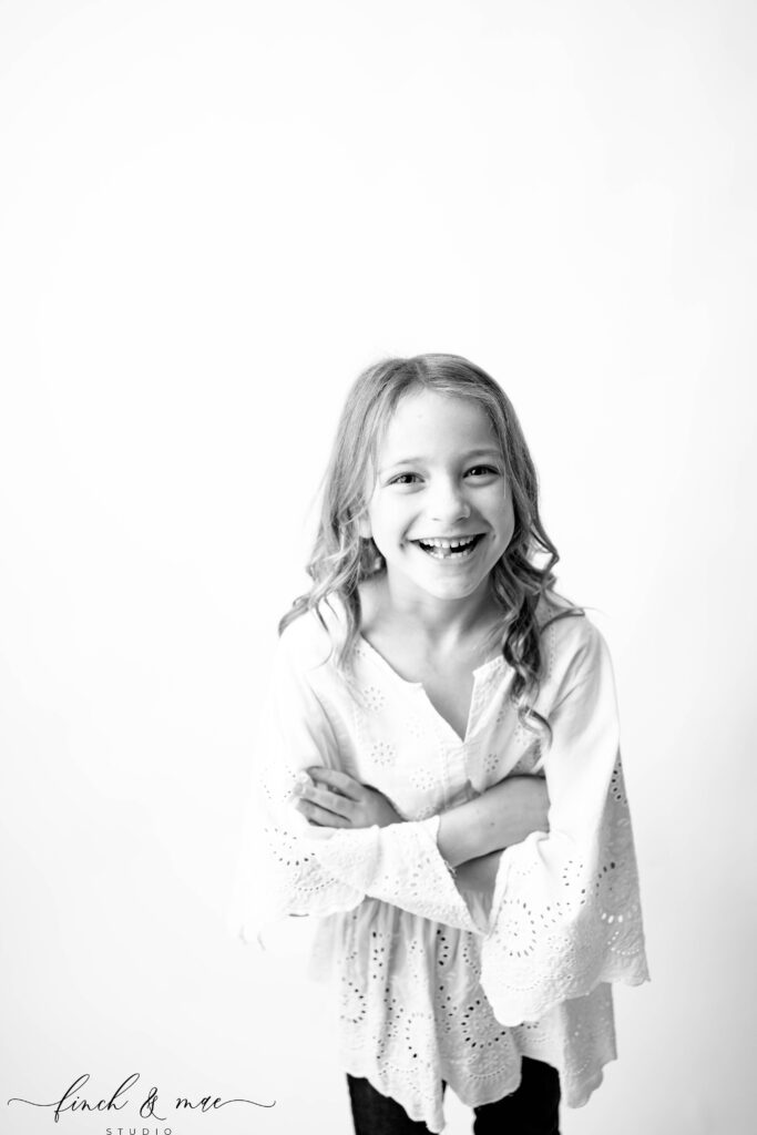 Joyful black and white photo of a girl with missing tooth smiling wide, personality portrait by Sun Prairie child photographer.