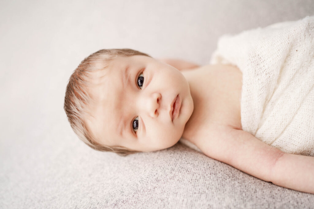 newborn boy laying on a cream backdrop
