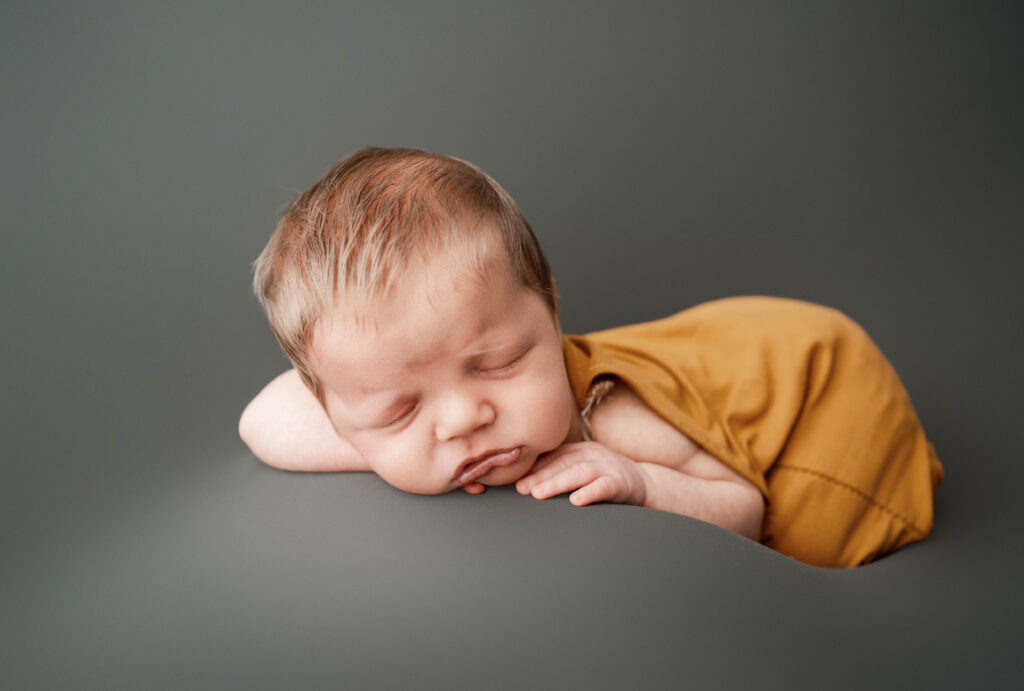 newborn baby boy wearing a yellow outfit while getting his newborn pictures taken in a rio, wi studio