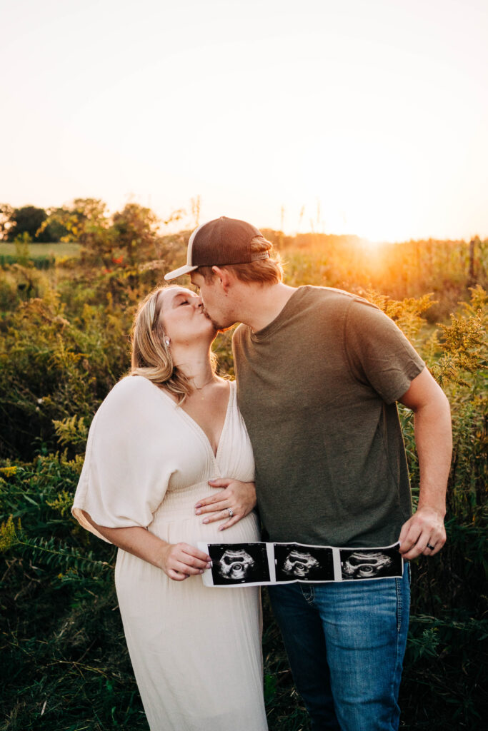 A couple kissing while Mom holds her belly and helps dad hold ultrasound pictures