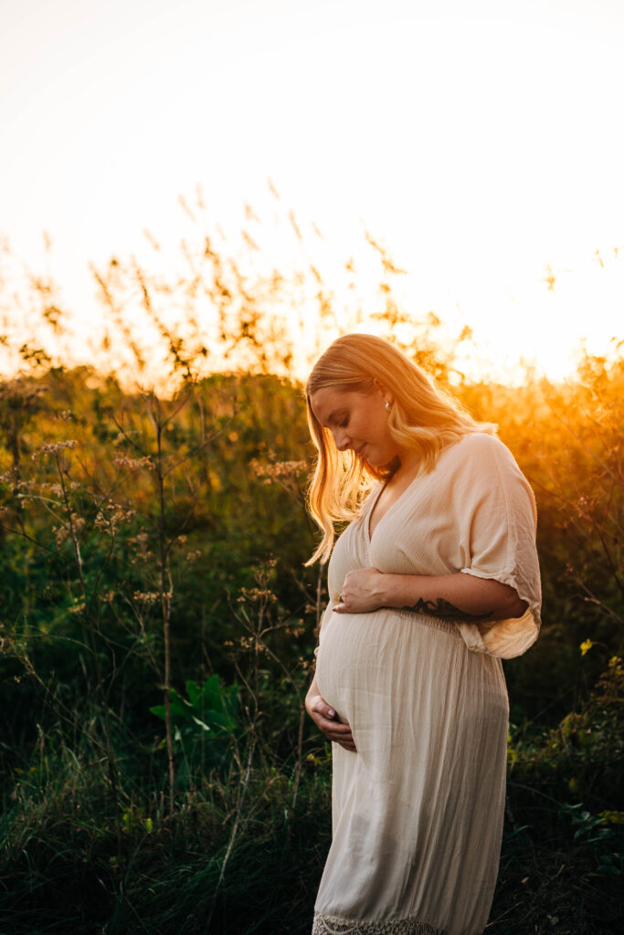 Expecting mother is basking in Wisconsin golden hour sun while crossing her expecting belly