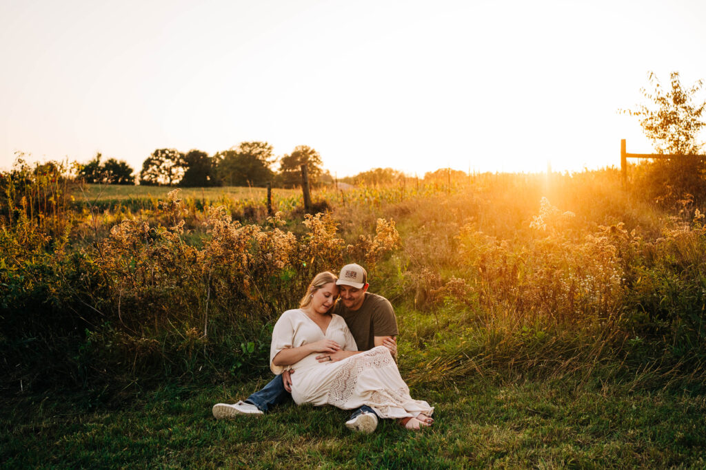 A couple is sitting in Wisconsin field while caressing an expecting belly