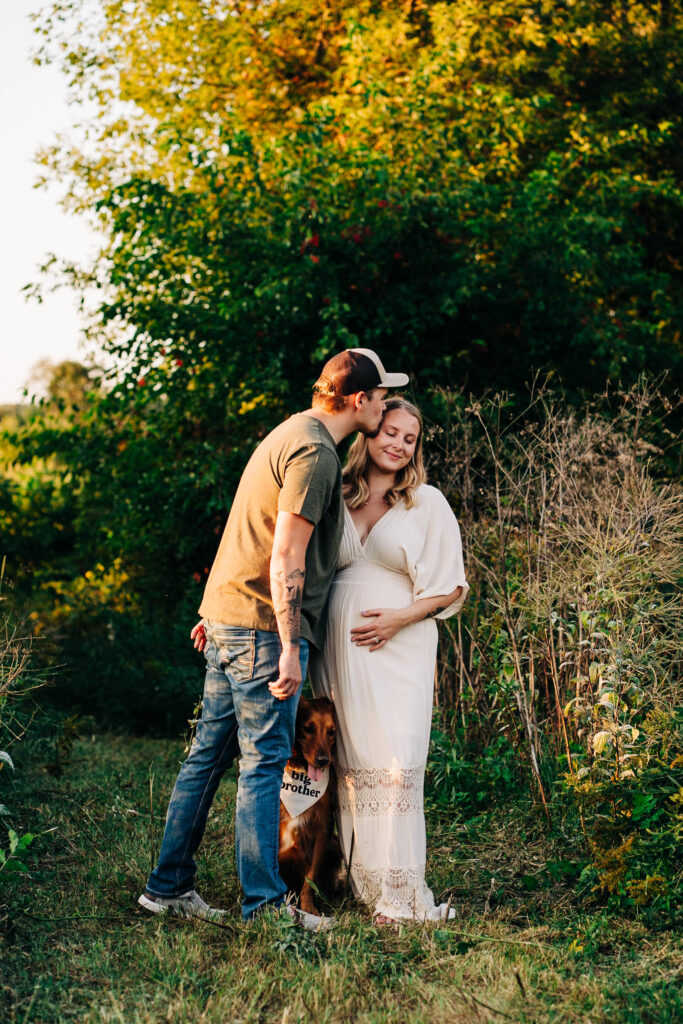Hey husband Temple while she holds her expecting belly and their golden retriever wears a bandanna that says big Brother