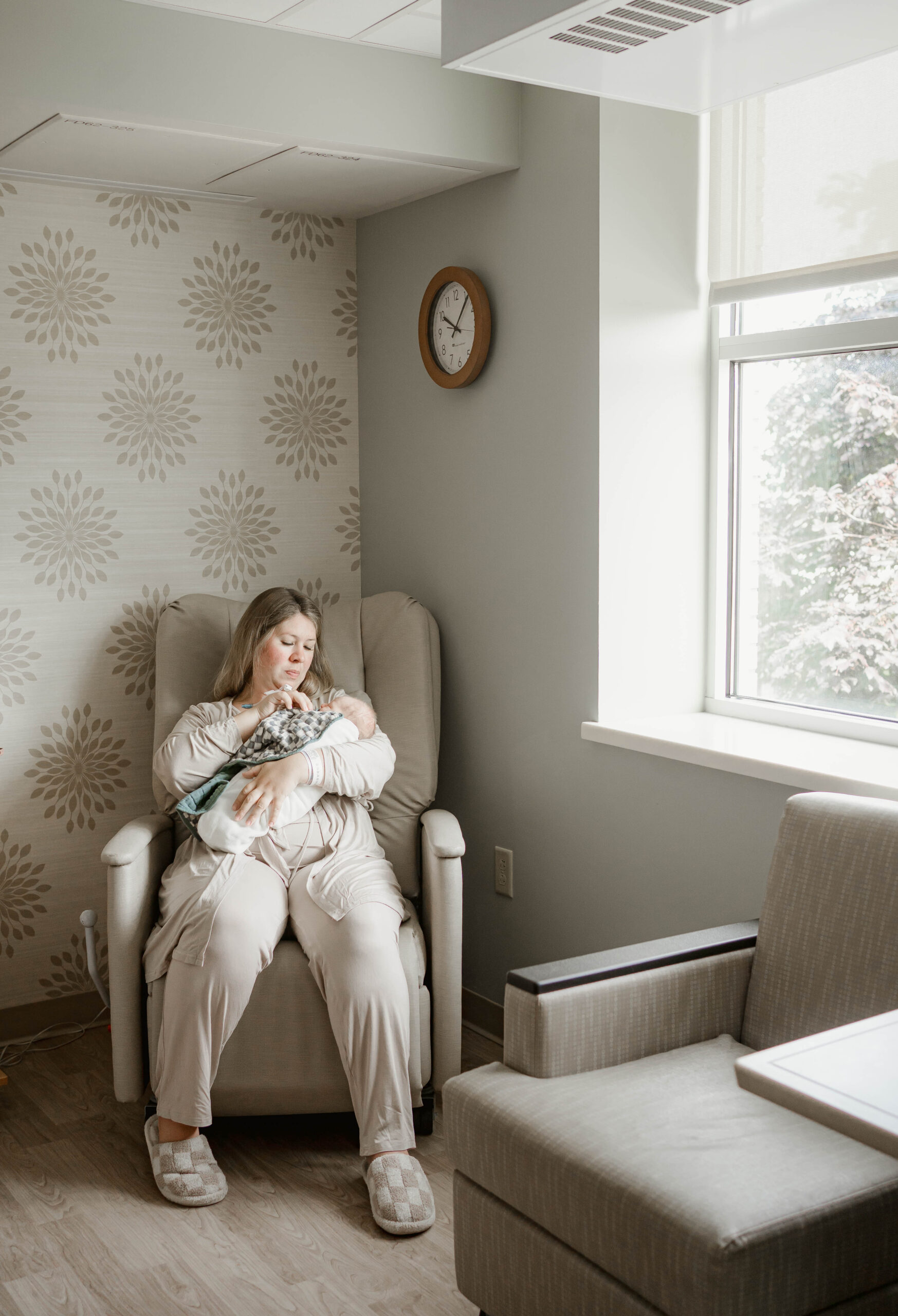 mom sitting in a hospital rocking chair with newborn son for fresh 48 session near milwaukee wi