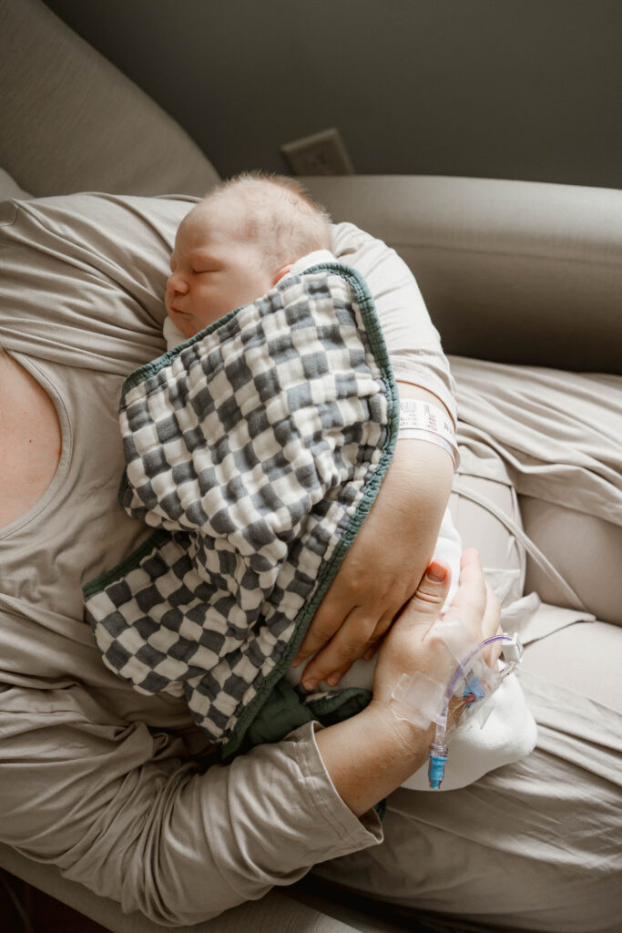 mom holding newborn son and is wrapped in a checkered blanket for a fresh 48 hospital session near madison