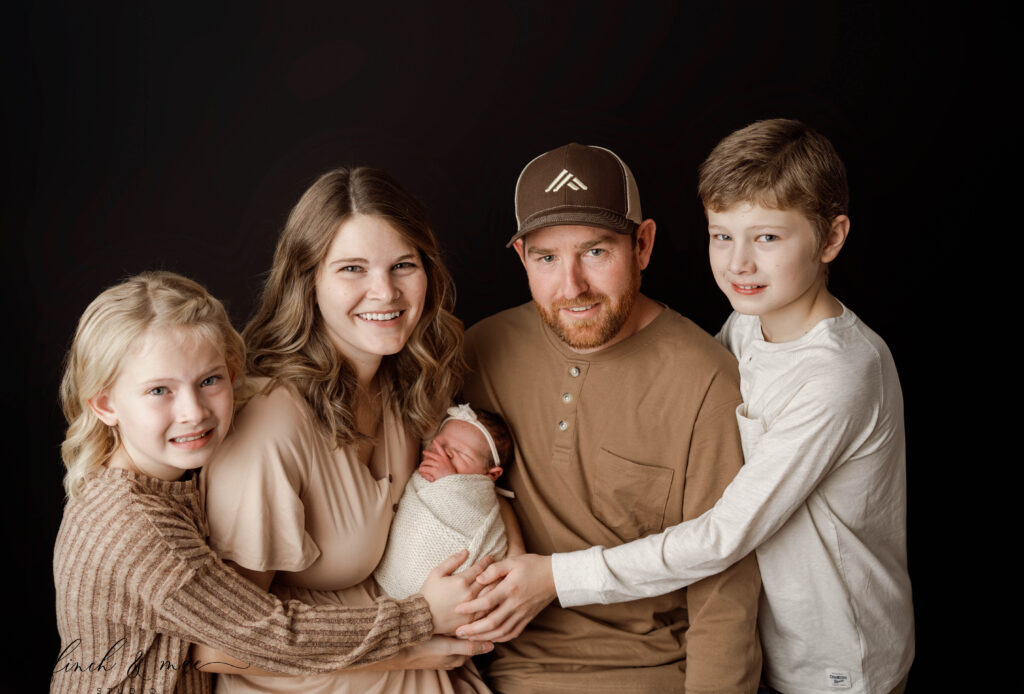 mom, dad, big sister and big brother all hold baby sister in newborn session in rio, wi studio