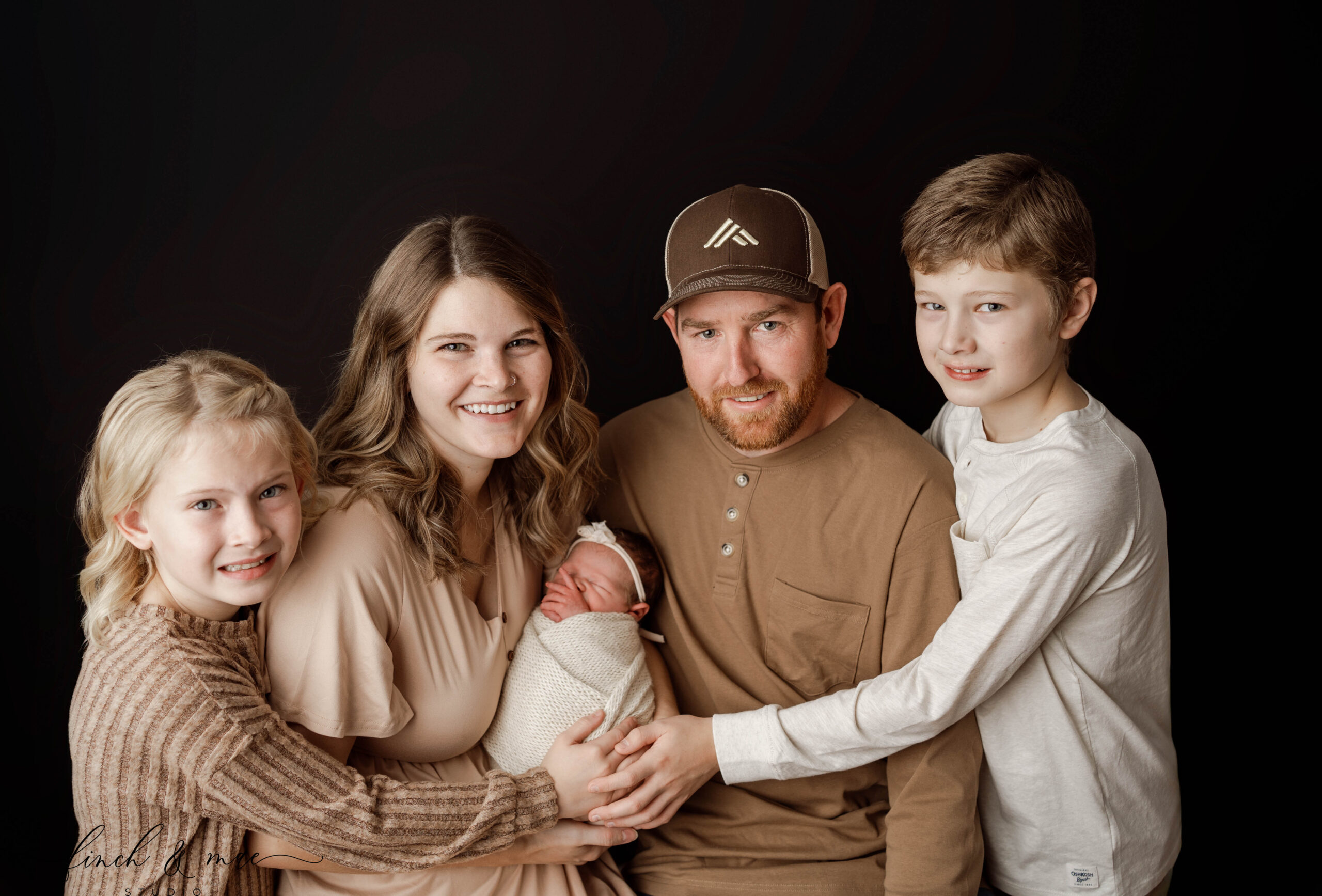 mom, dad, big sister and big brother all hold baby sister in newborn session in rio, wi studio