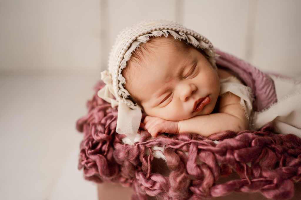 Newborn baby girl in a purple box wearing a white bonnet in Rio, Wisconsin newborns portrait, Studio
