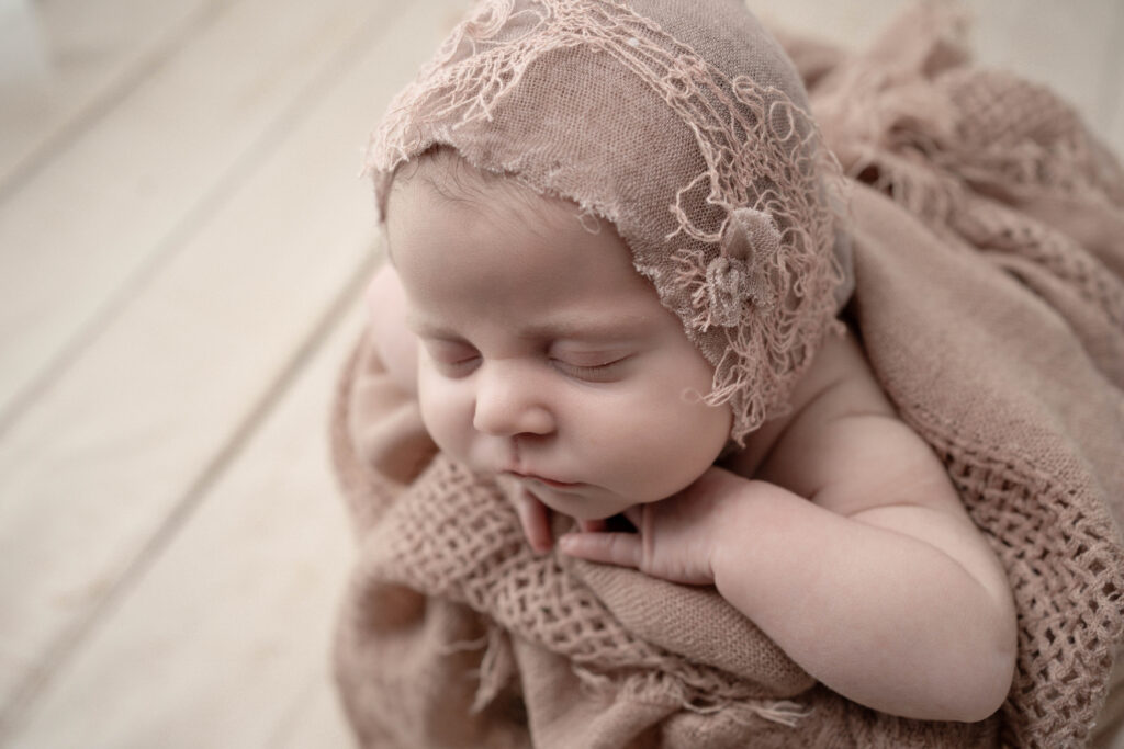 newborn wrapped in a a textured fabric with bonnet on neutral backdrop