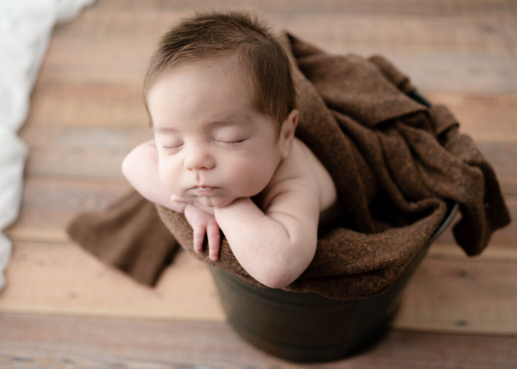 newborn boy in a metal bucket sleeping