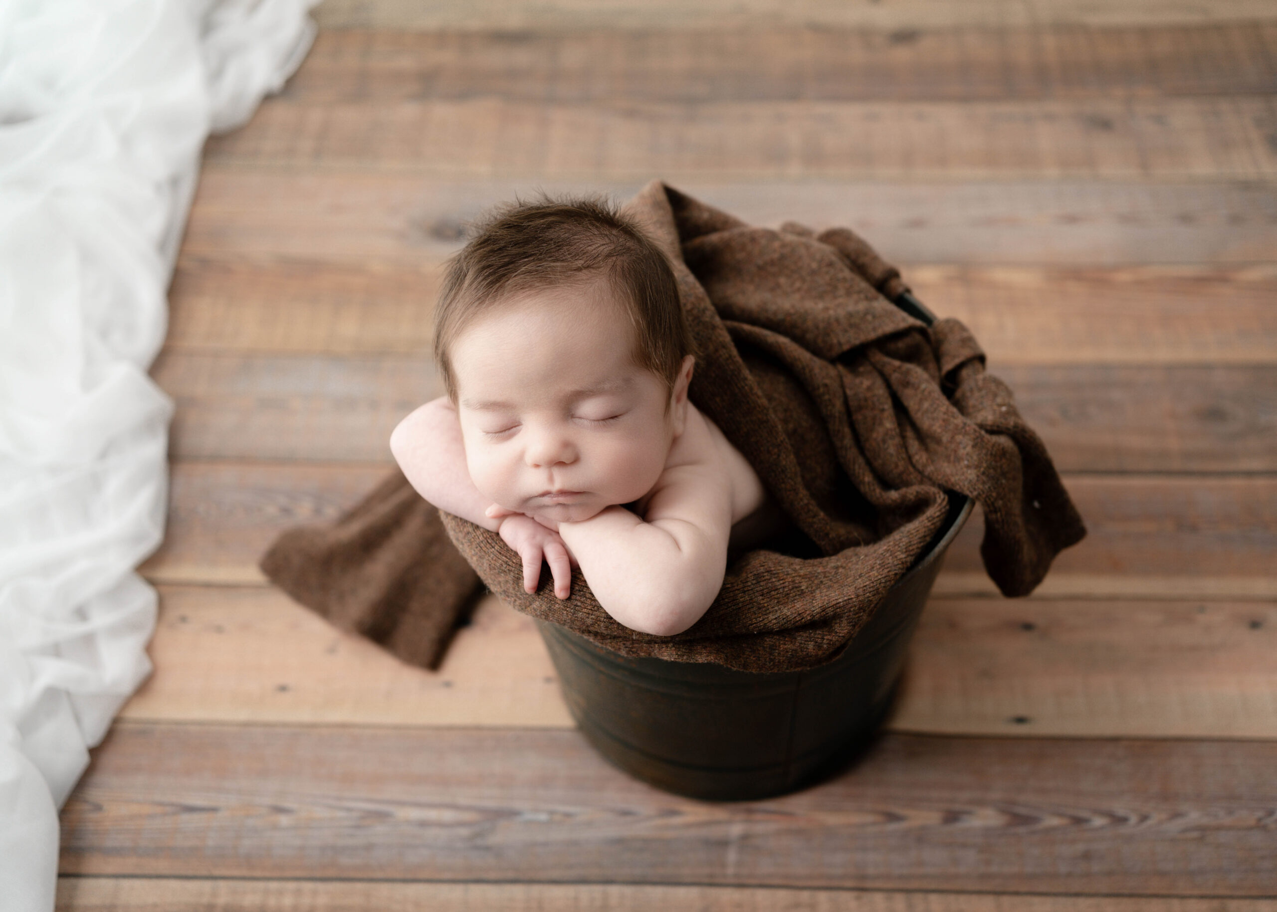 sleeping newborn boy in a metal brown bucket on a wooden floor