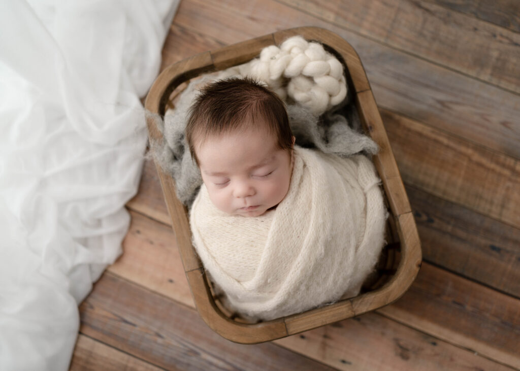 newborn boy in wooden basket with soft textures on a wooden floor
