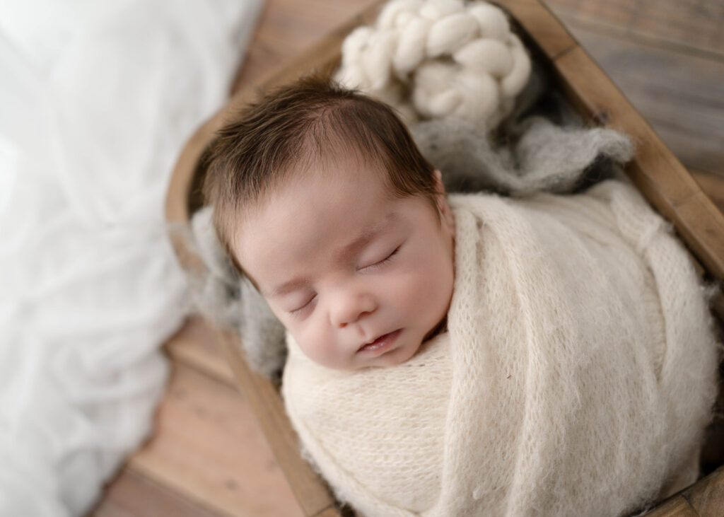 newborn baby in wooden basket with soft textures