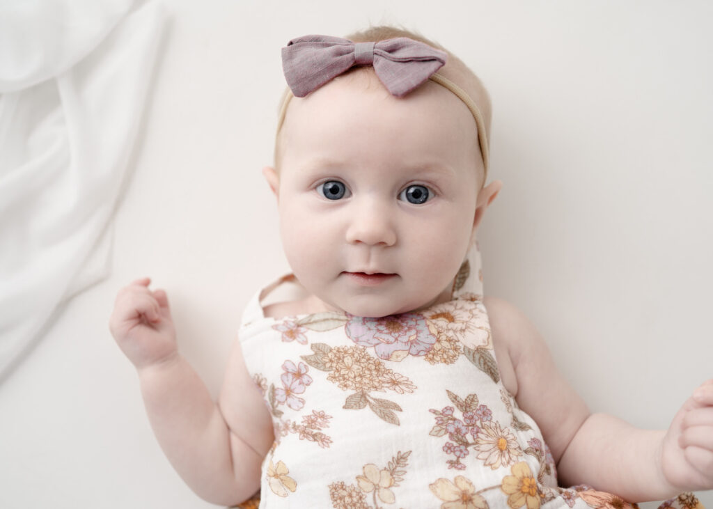 Six-month milestone portrait of baby girl wearing a floral romper and bow headband at Finch & Mae Studio.