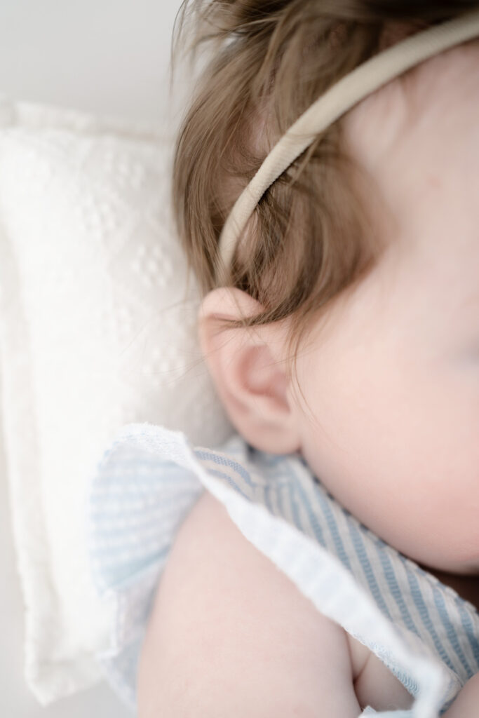 Close-up detail photograph of baby girl’s cheek, headband, and ruffle sleeve during a milestone photography session.