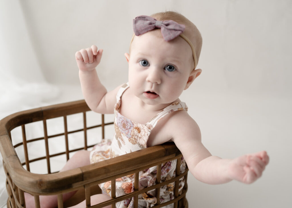 Baby girl standing with support in a vintage basket during a milestone photography session in Rio, Wisconsin.
