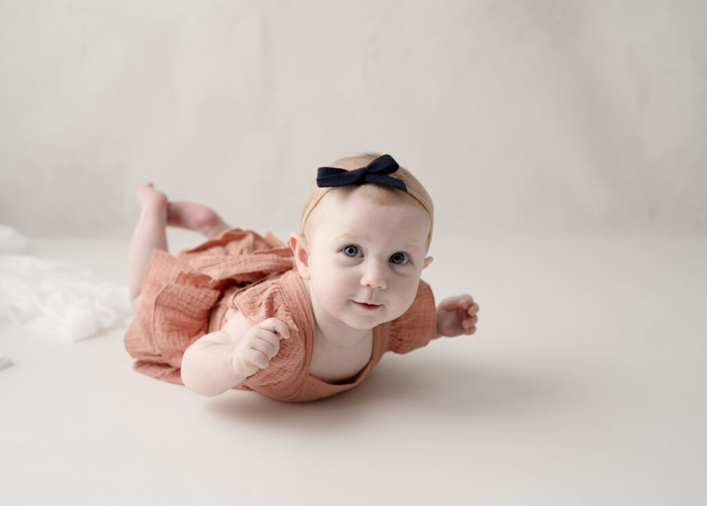 Baby girl practicing tummy time on a neutral studio backdrop during a milestone portrait session.