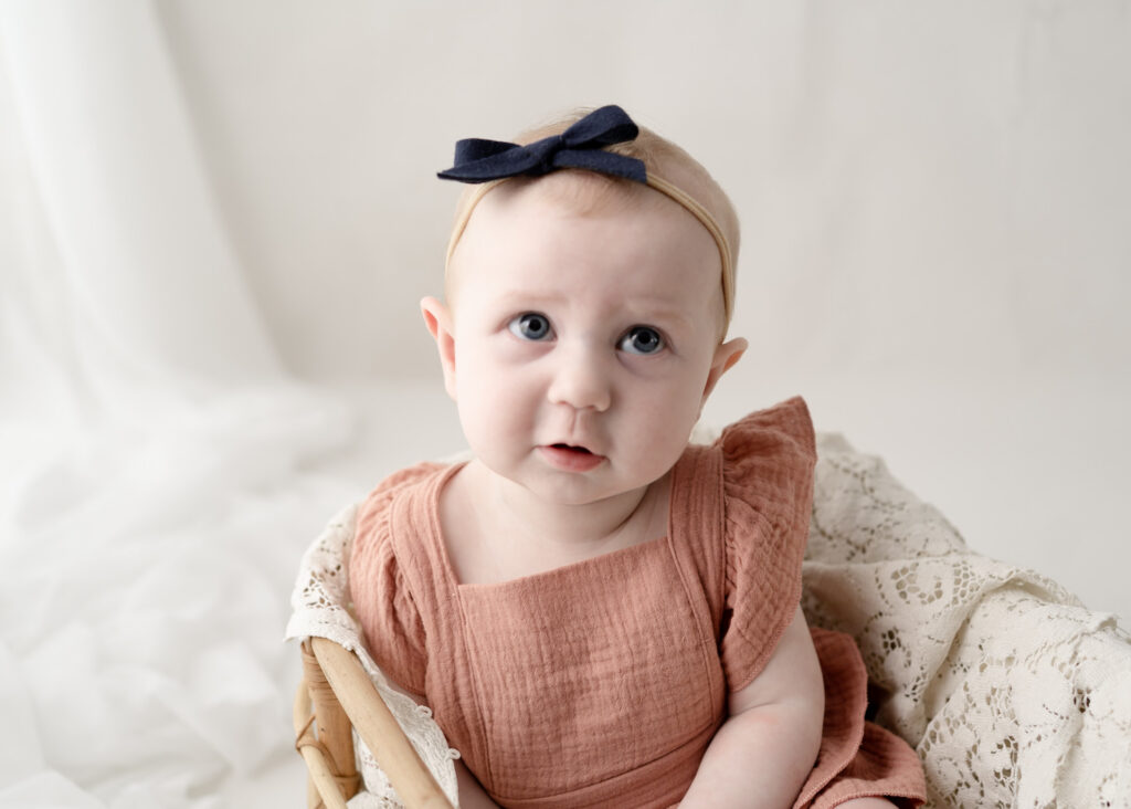 Baby girl sitting independently and smiling during a six-month milestone session at a Wisconsin photography studio.
