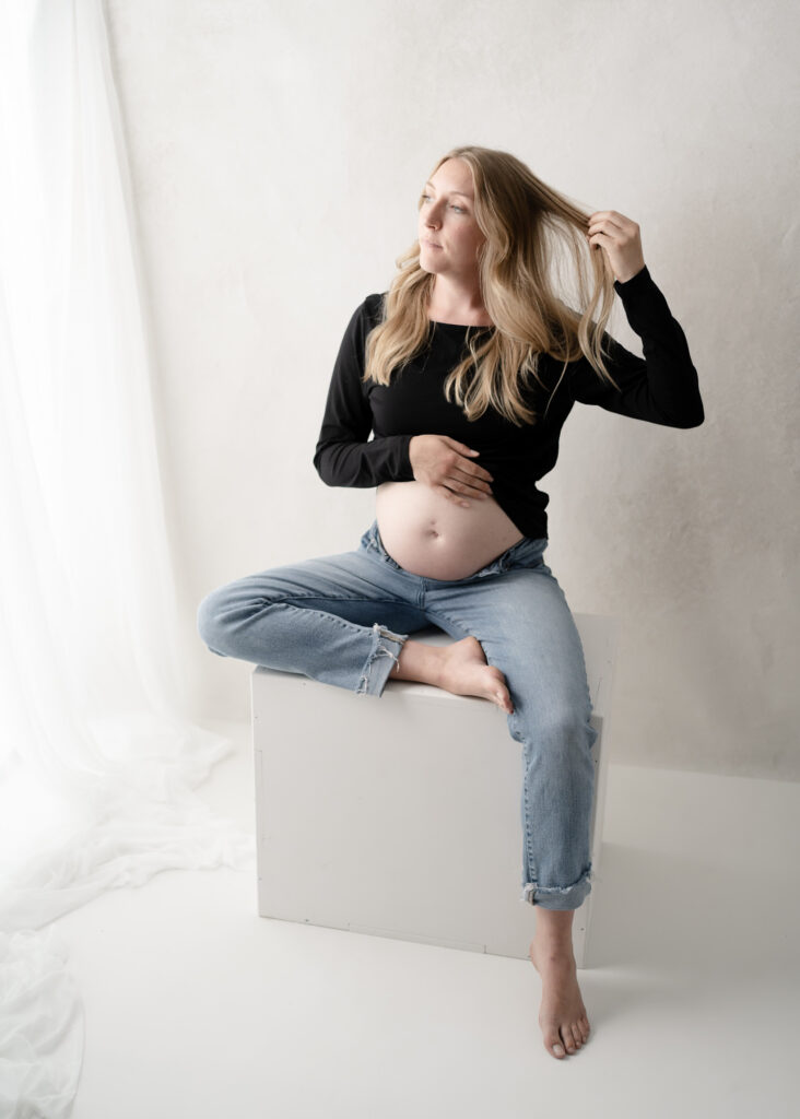 Studio maternity portrait of expectant mother seated on a white posing cube during a maternity photography session in Rio, Wisconsin.