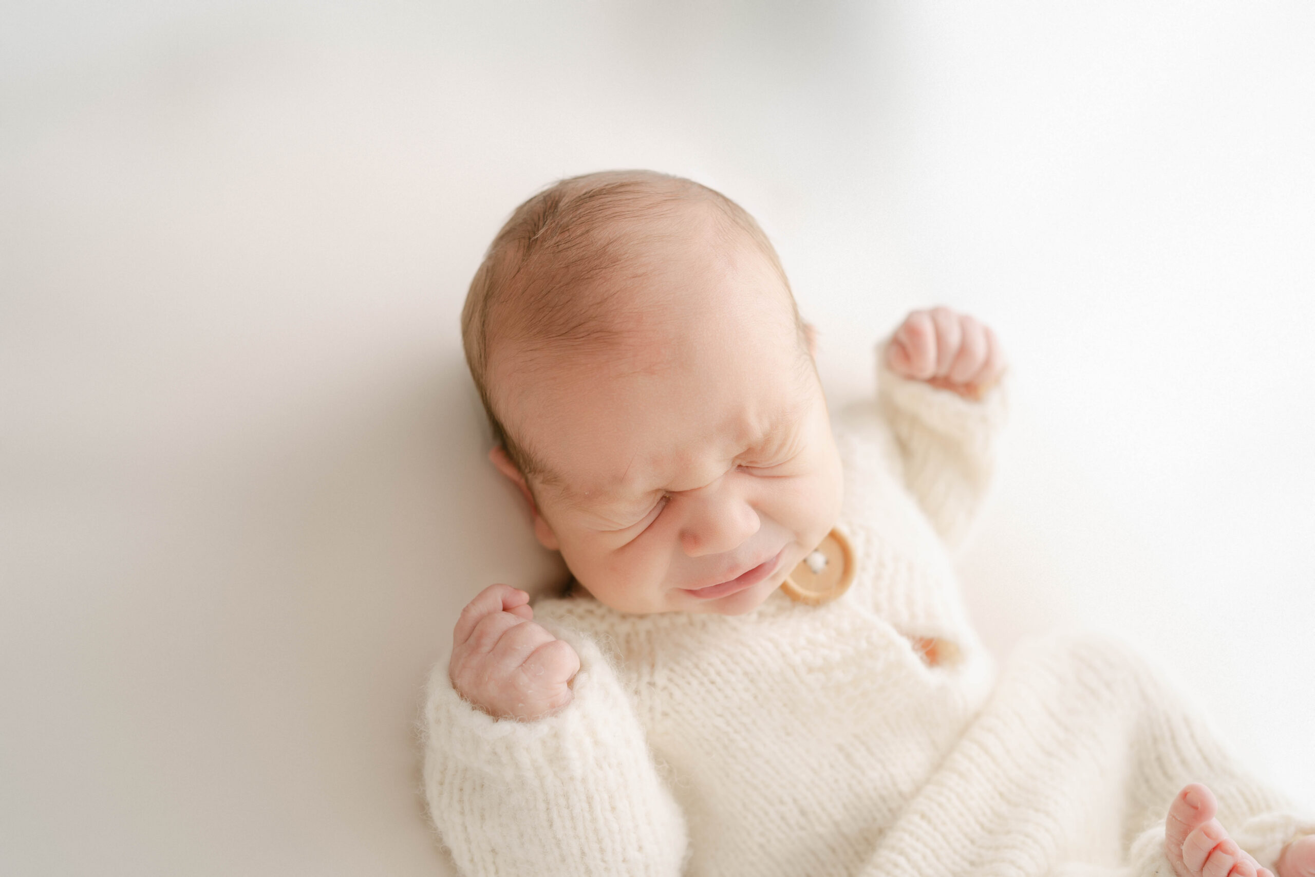 Baby in cream sneezing in Rio, WI newborn studio.