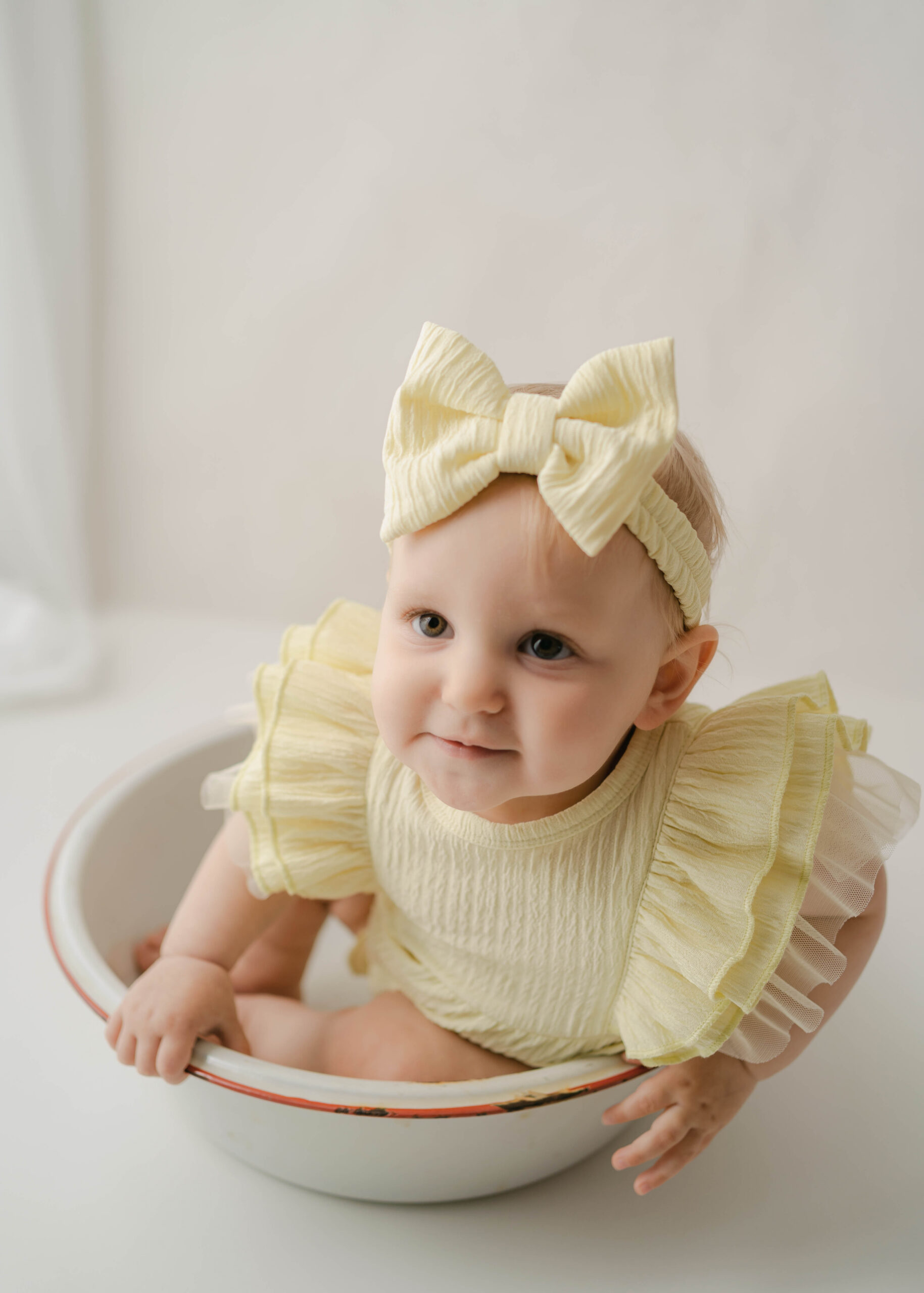 One year old in a yellow outfit sitting in a metal bowl for one year portraits in rio, wi