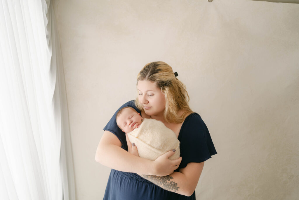 mom is wearing a blue dress and is holding newborn son for newborn portraits near sun prairie wi