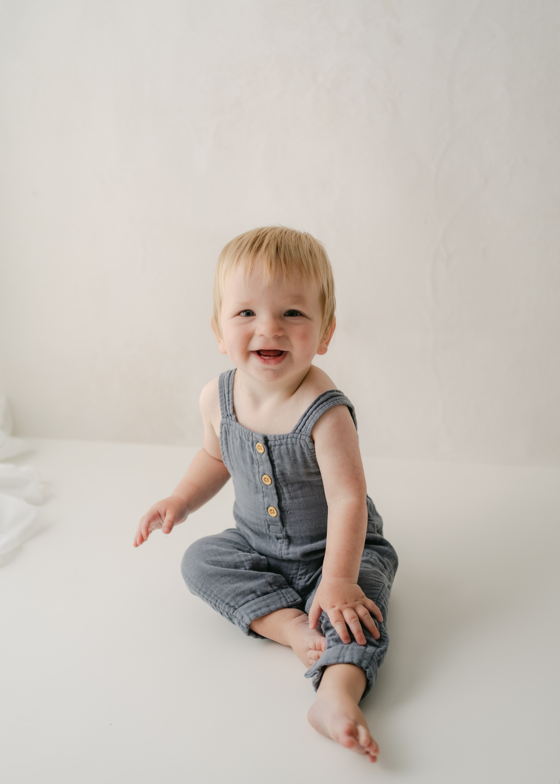 11 month old boy sitting in portrait, Studio wearing blue overalls