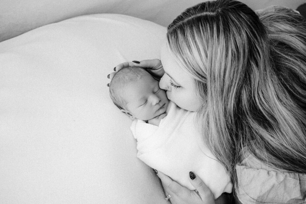 black and white image of mom kissing newborn son's cheek near madison, wi