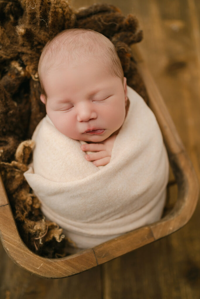 sleeping newborn with brown textures in a wooden basket - Newborn photography session near Madison, WI